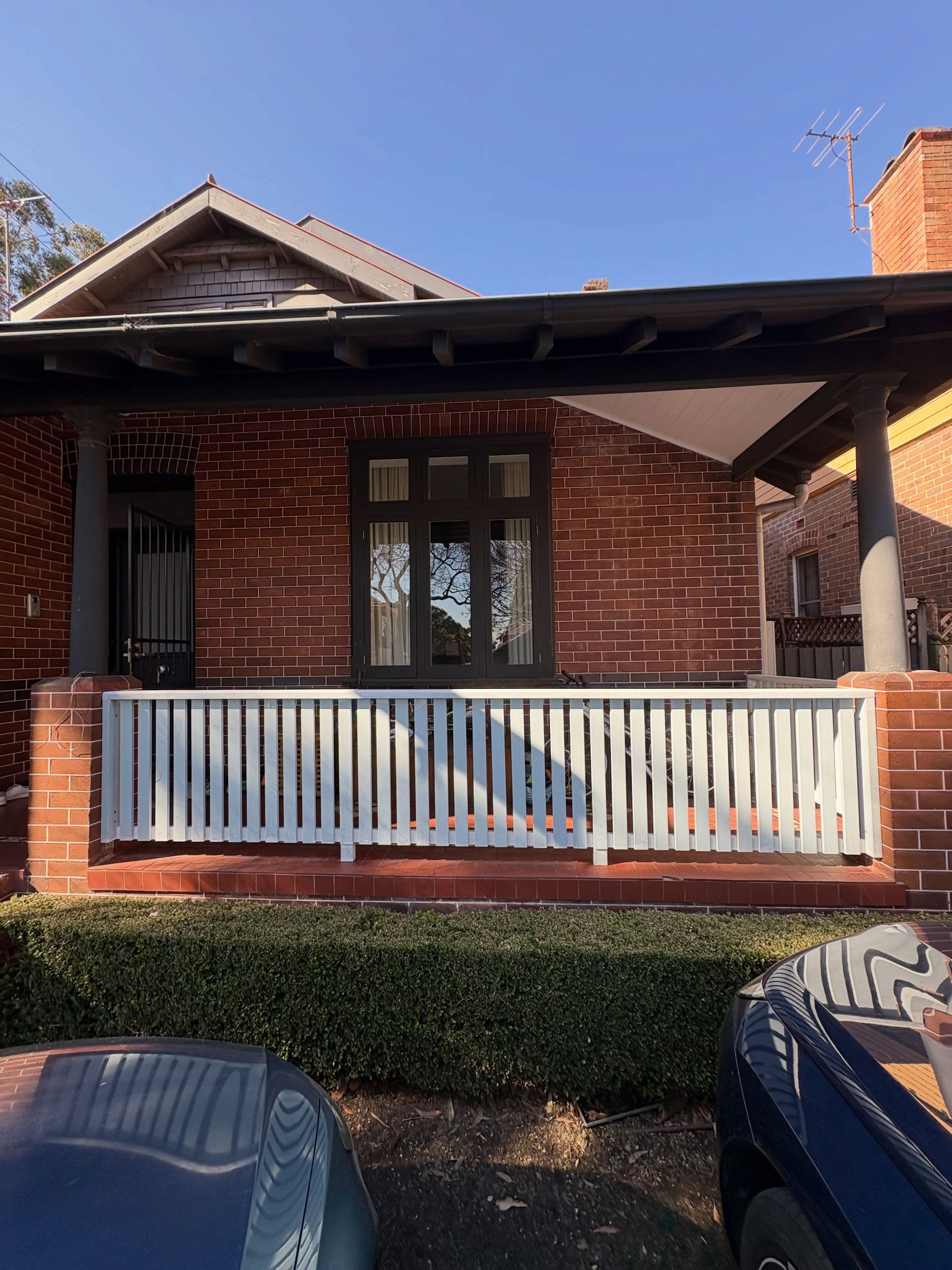 Brick house with white porch railing and columns, viewed from the front in daylight.