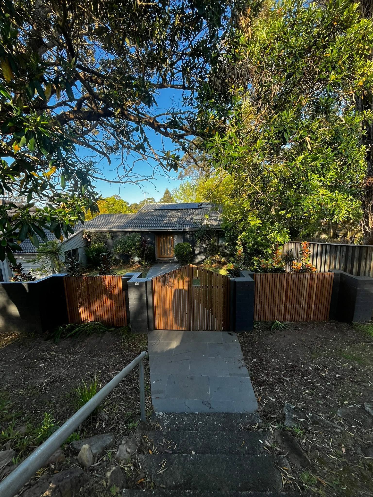 Leafy backyard with a wooden fence, small ramp, and a house partially visible through trees.