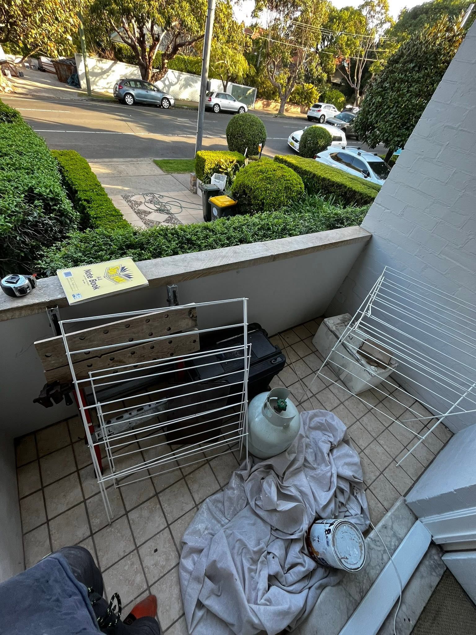 Balcony with drying rack, crumpled towel, and gas cylinder overlooking a street and parked cars