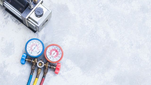 Refrigeration gauges and pump on a gray textured surface, showing pressure readings.