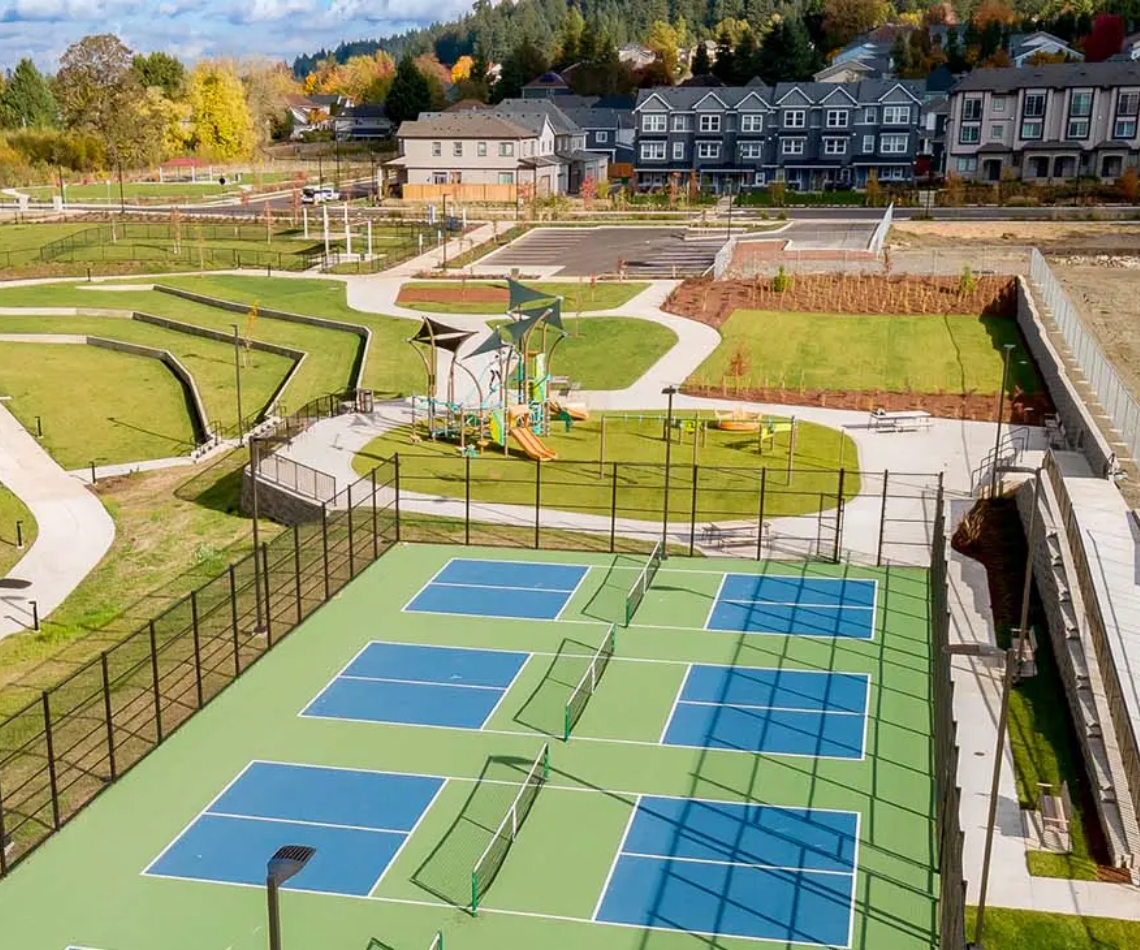 Outdoor sports complex with blue pickleball courts, grassy terraces, and a clubhouse in the background