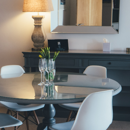 Modern dining room with round glass table, white chairs, vase of flowers, and a lit floor lamp