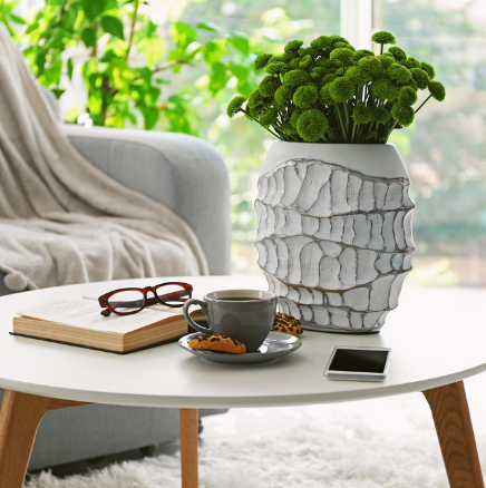 Modern living room table with a white vase of greenery, coffee cup, book, glasses, and smartphone