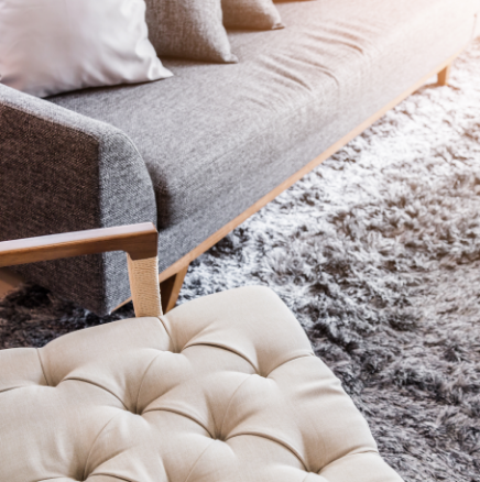 Modern living room with gray sofa, wooden frame, and beige tufted ottoman on a shaggy rug