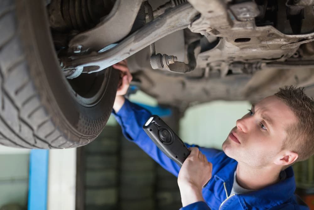 A Man Is Looking Under A Car With A Flashlight — Banora Automotive In Tweed Heads South, NSW