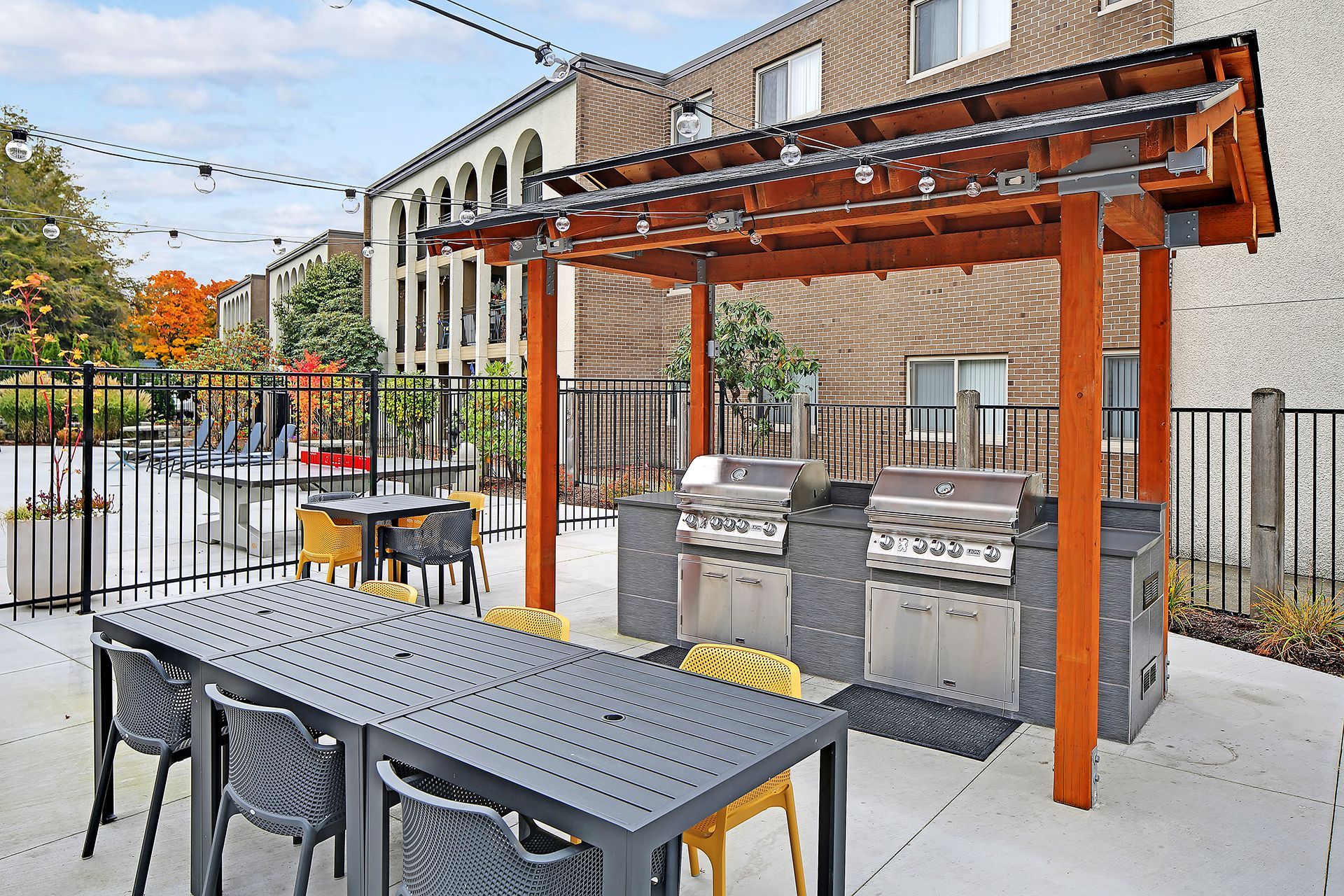 A patio with a table and chairs and a grill under a pergola.