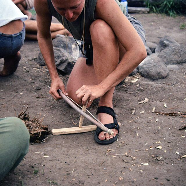 A woman is kneeling down in the dirt using a saw