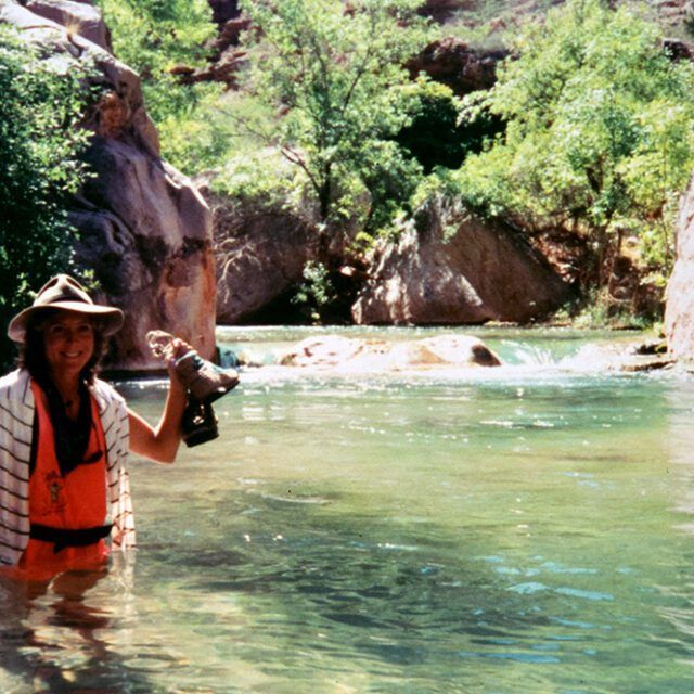 A woman is standing in a river holding a camera