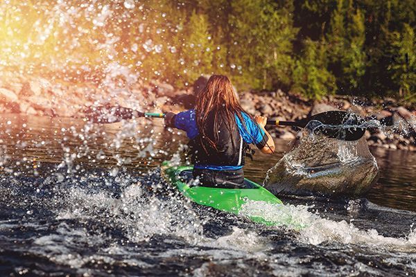 A woman is paddling a green kayak down a river.