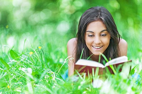 A woman is laying in the grass reading a book.
