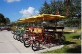 A row of bicycles with umbrellas are parked on the side of the road.