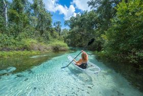 A woman is paddling a clear kayak down a river.