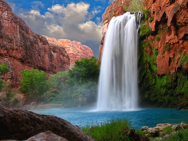 A waterfall is surrounded by trees and rocks in the middle of a canyon.