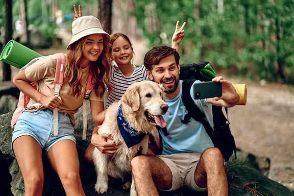 A family is taking a selfie with their dog in the woods.