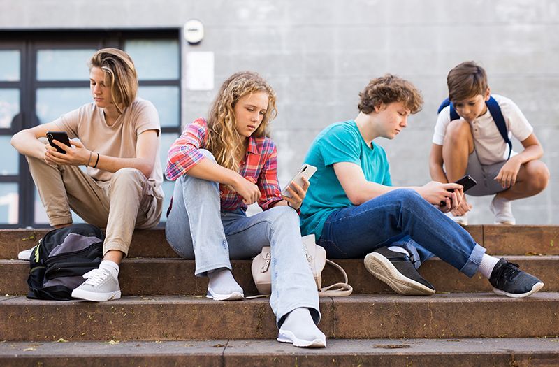 A group of young people are sitting on the steps of a building looking at their phones.