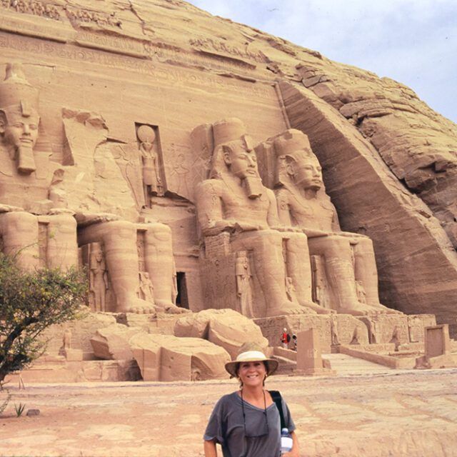 A woman in a hat stands in front of a large statue