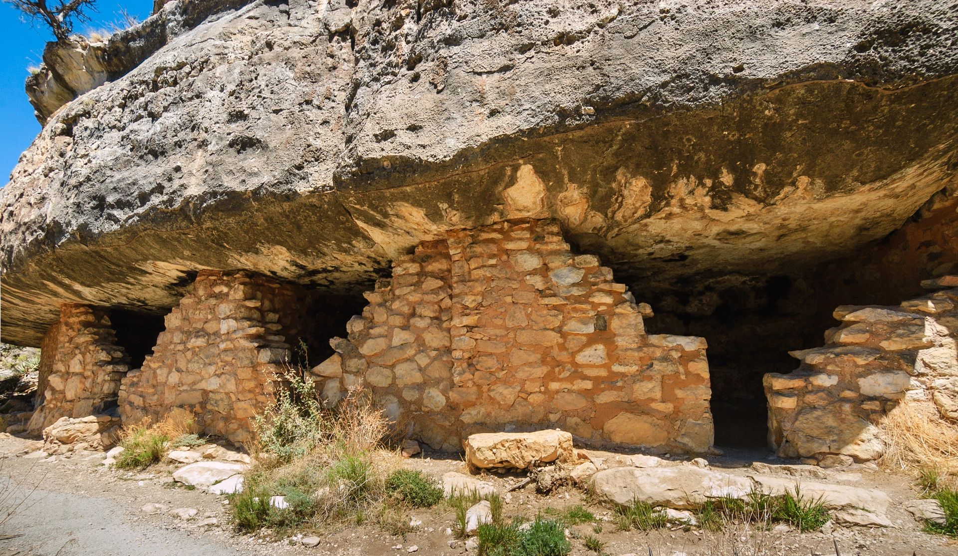 A stone building is sitting under a large rock.