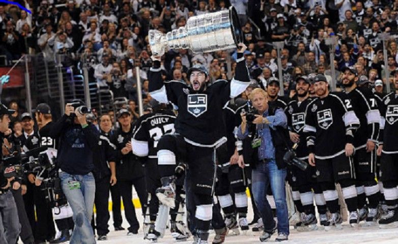 a hockey player from te LA Kings is holding a trophy over his head in front of a crowd .