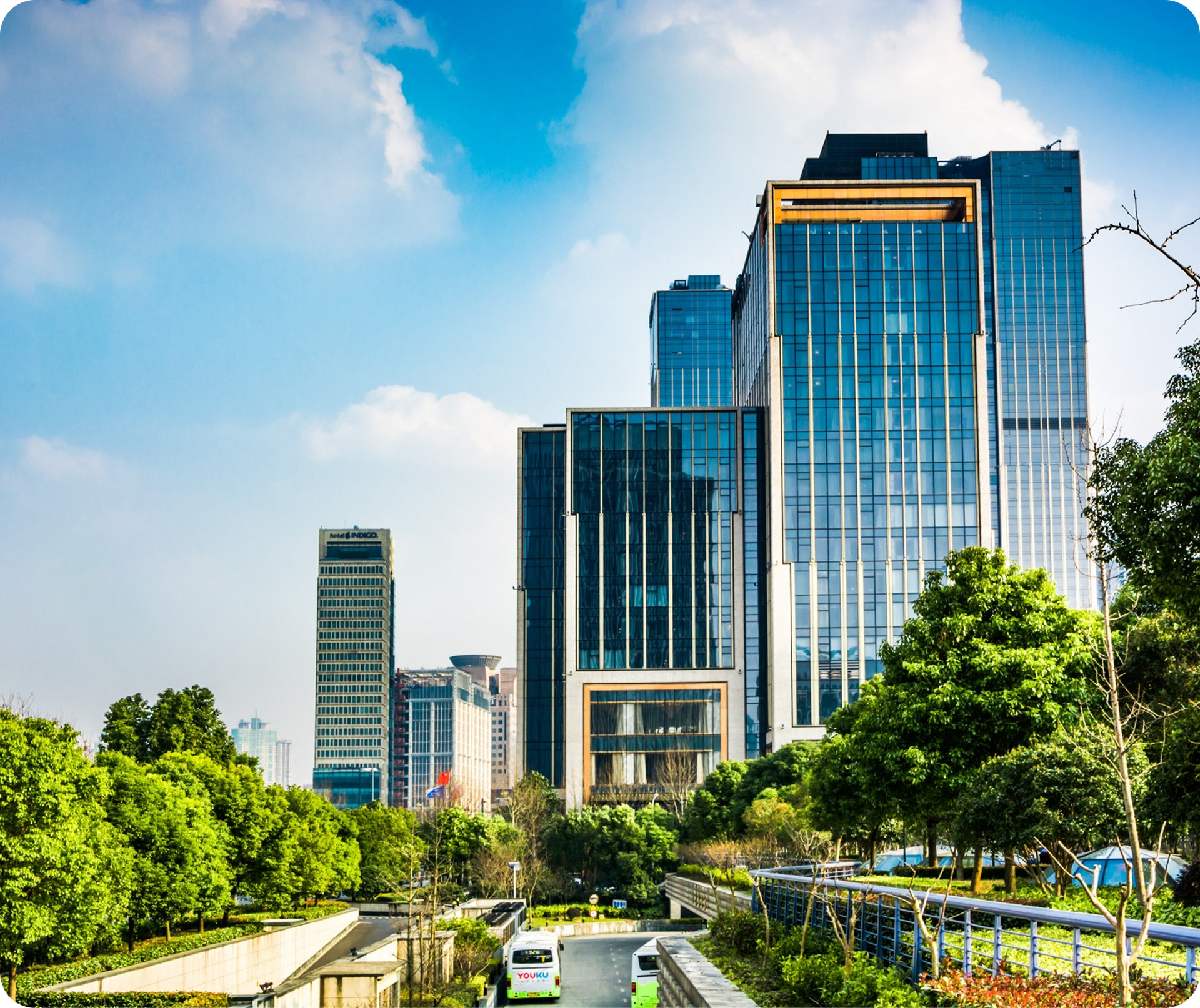 Modern glass office towers in a green cityscape under a blue sky