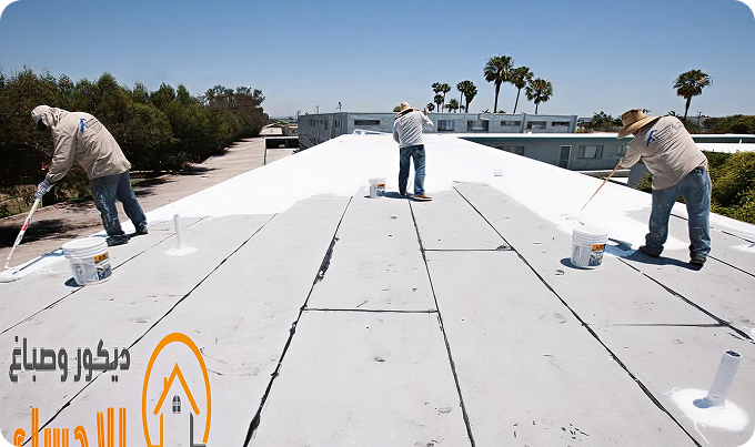 Workers installing white roofing membrane on a flat rooftop under a clear blue sky