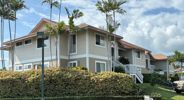 Two-story tan building with wraparound balcony and palm trees under a clear blue sky
