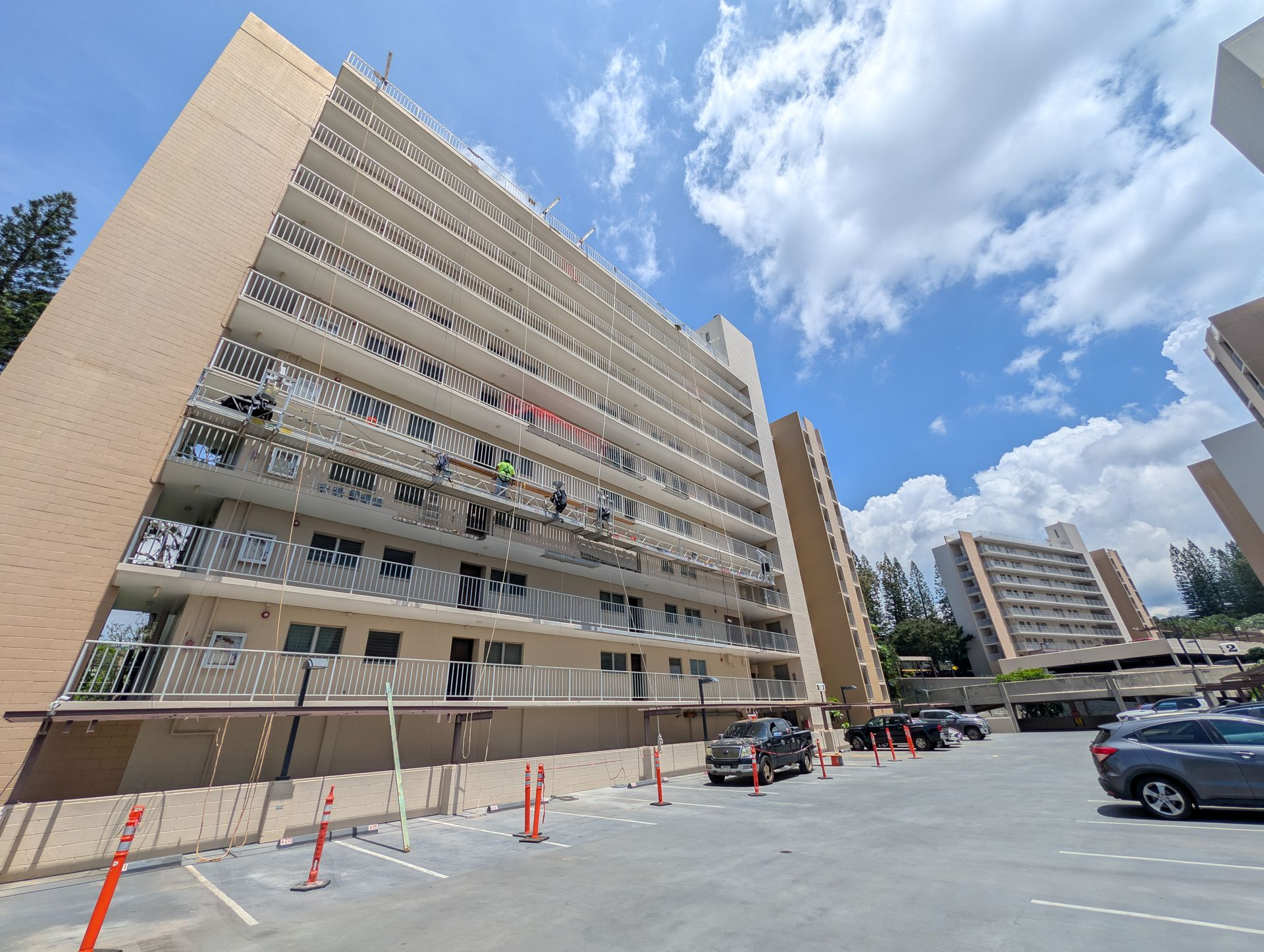 Worker on a lift spraying beige coating onto an exterior wall near a gray section