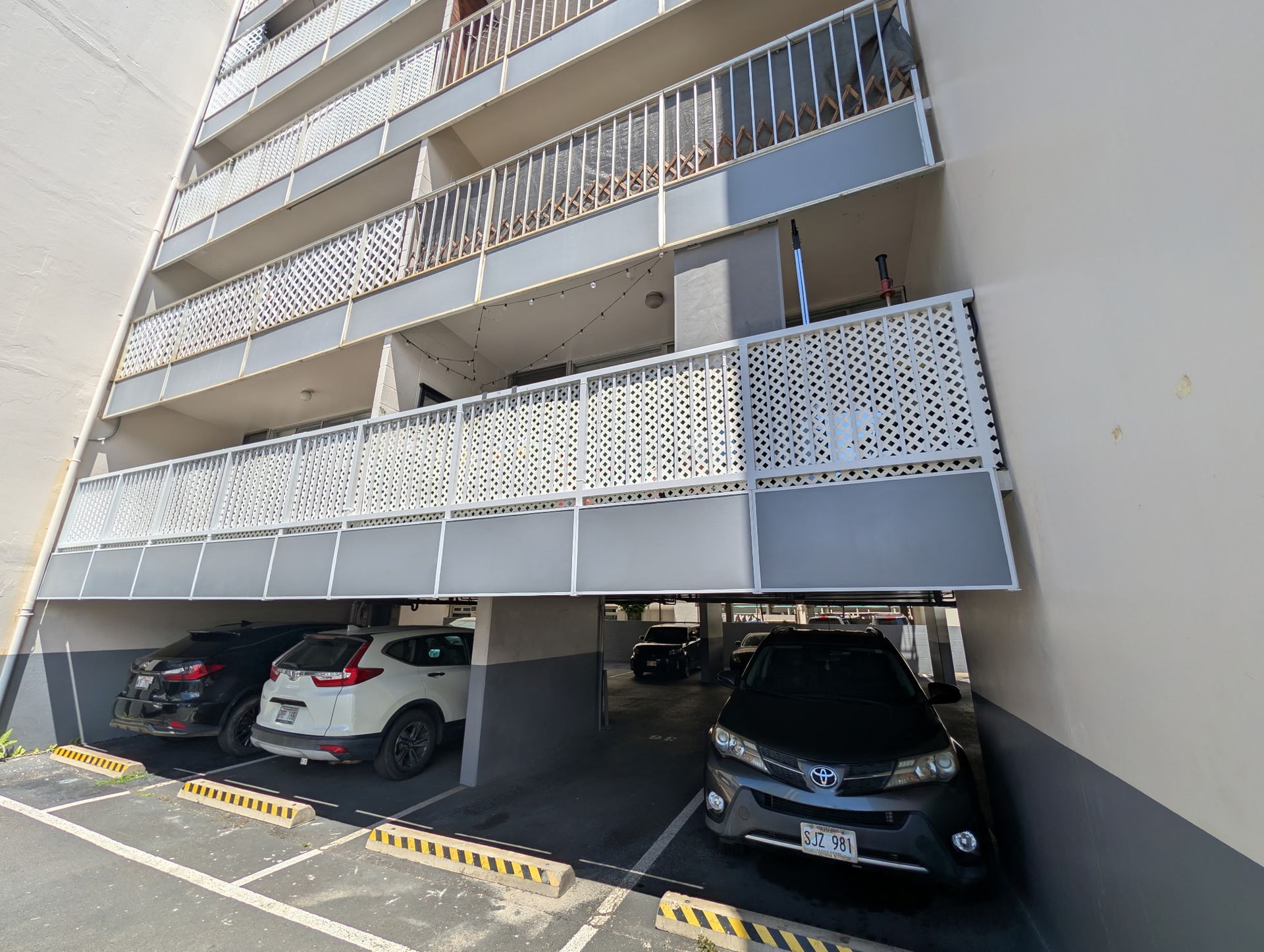 Covered apartment parking garage with several parked cars and white lattice balconies above