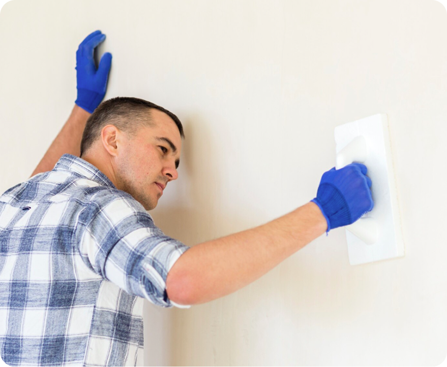 Worker in blue gloves smoothing a white wall with a putty knife