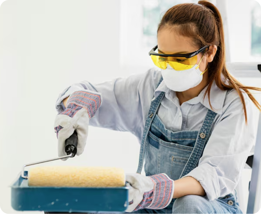 Person in safety gear painting a wall with a paint roller indoors.
