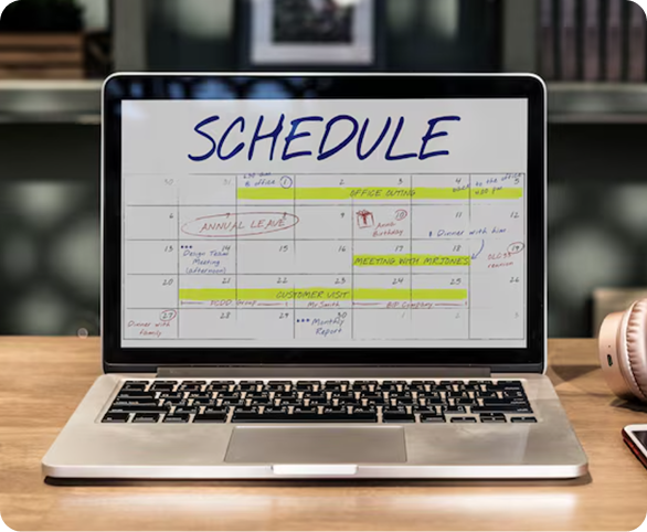 Laptop on desk showing a weekly schedule on screen in a bright office setting