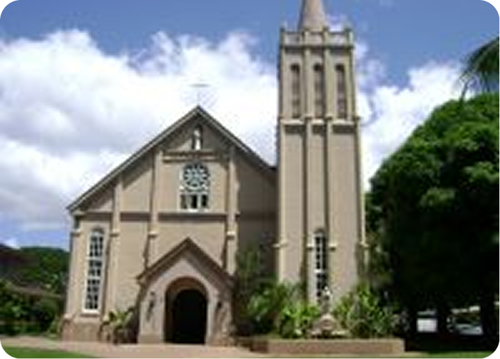 Exterior of a beige church with a tall bell tower and arched entrance under a partly cloudy sky