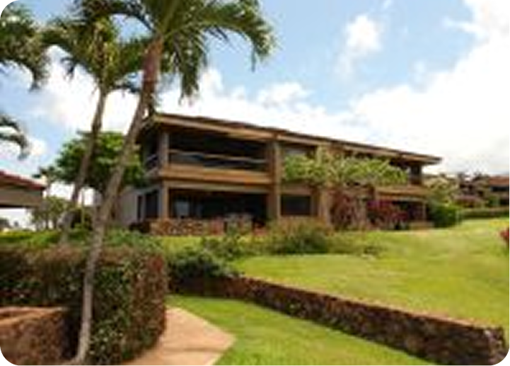 Tropical resort building with a manicured lawn, palm trees, and ocean view under a partly cloudy sky