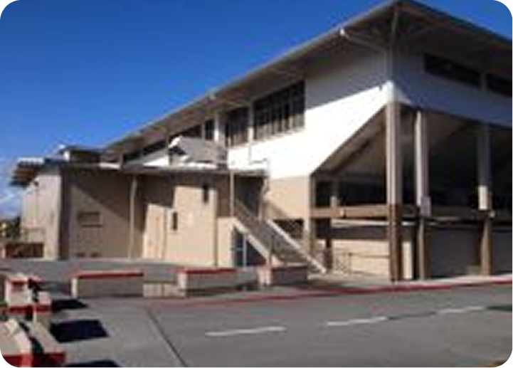 Modern building with beige walls and white overhangs beside a parking lot under a blue sky