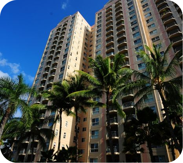 Tall beige high-rise apartments with palm trees against a bright blue sky