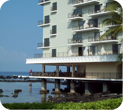 Seaside hotel building on stilts beside rocky shoreline and calm blue water
