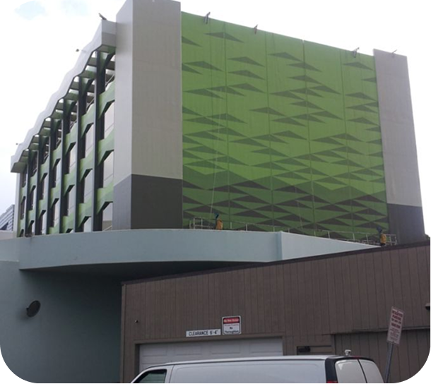 Green-and-gray multi-story parking structure with a curved lower facade and a van parked below