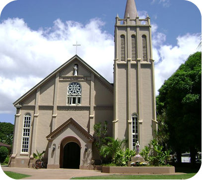 Small beige church with a tall steeple and arched entrance under a blue sky with clouds.