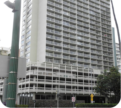 Tall white high-rise building with balconies and ground-level parking, viewed from the street.
