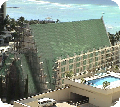 Building under construction wrapped in green netting beside a rooftop pool and palm trees