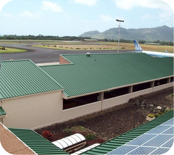 Green-roofed building beside an airport runway with mountains in the background