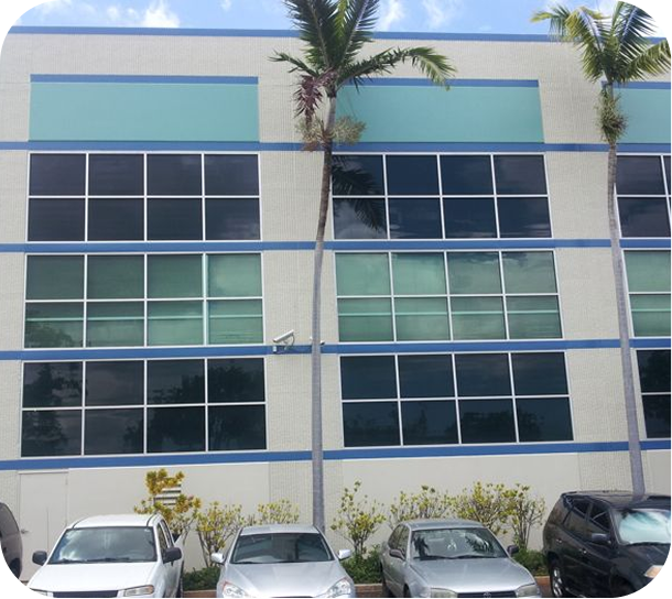 Modern three-story office building with blue-tinted windows, palm trees, and parked cars in front