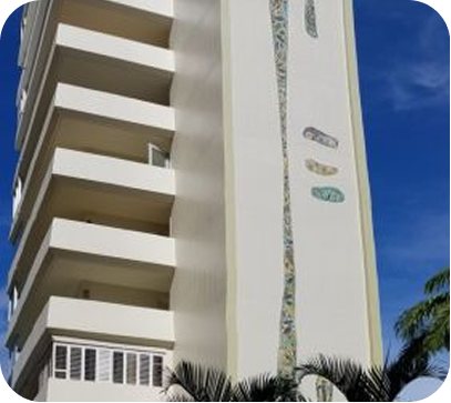 Tall white modern building with balconies against a blue sky and palm fronds below
