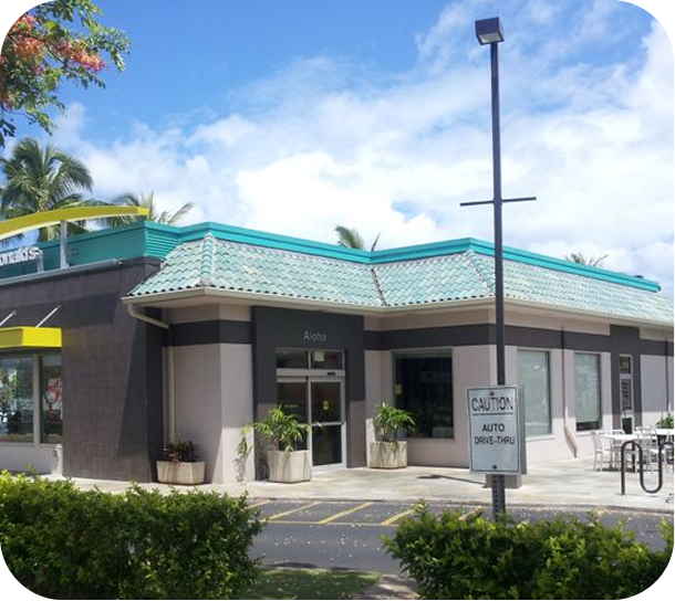 Low-rise storefront with teal roof, gray walls, and a sign by the entrance on a sunny day
