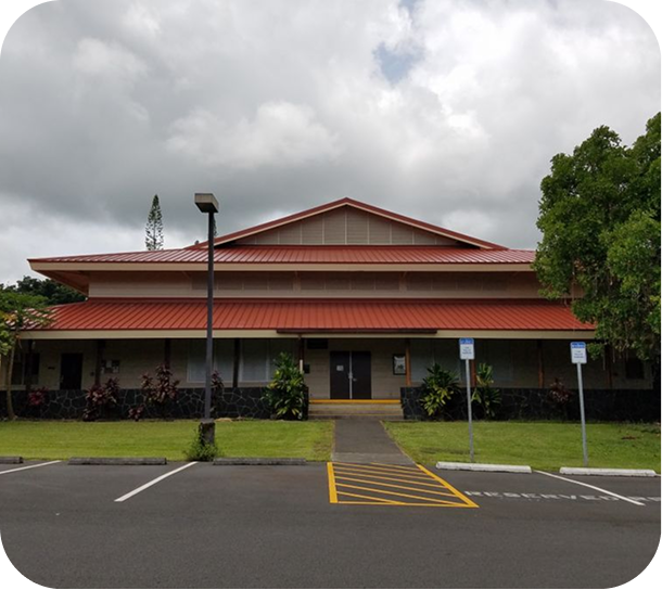 Low red-roofed building with covered entrance, parking lot, and cloudy sky