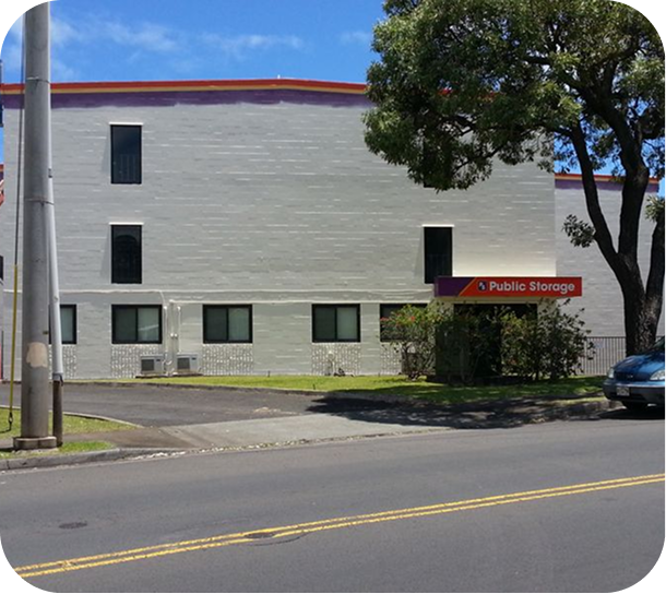 Public storage building with a red sign beside a street and parked car