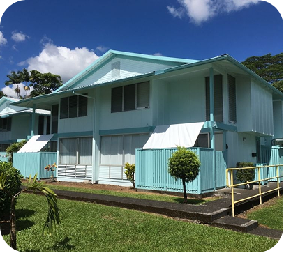 Light blue two-story house with a green roof, white trim, and a grassy yard under a sunny sky
