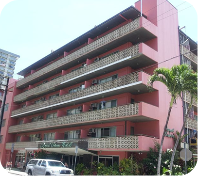 Pink multi-story building with balconies, palm trees, and parked cars on a street