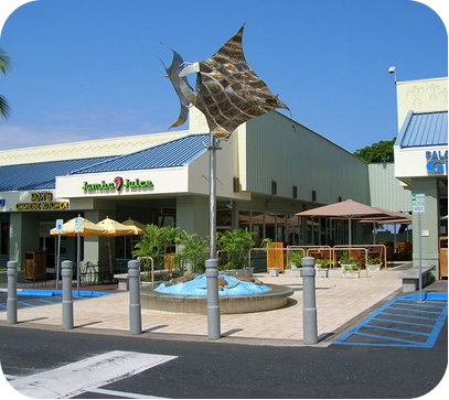 Outdoor shopping center with fountain, umbrellas, and a large decorative shark sculpture above the entrance
