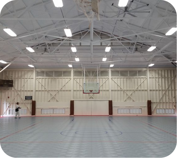 Empty indoor gymnasium with a basketball hoop and high white ceiling lights