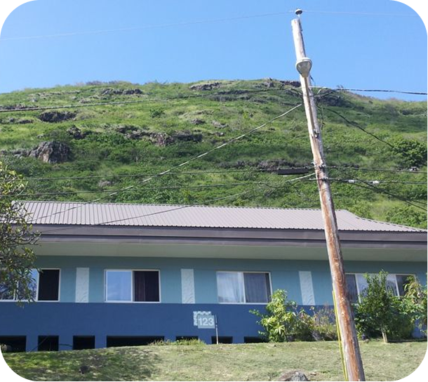 Blue building at the base of a green hillside, with a leaning utility pole in the foreground.